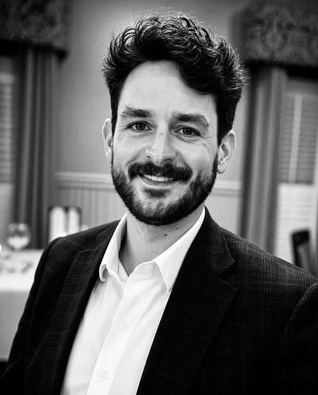 Black-and-white portrait of Gus Guidry, smiling, in a dark blazer and white shirt.